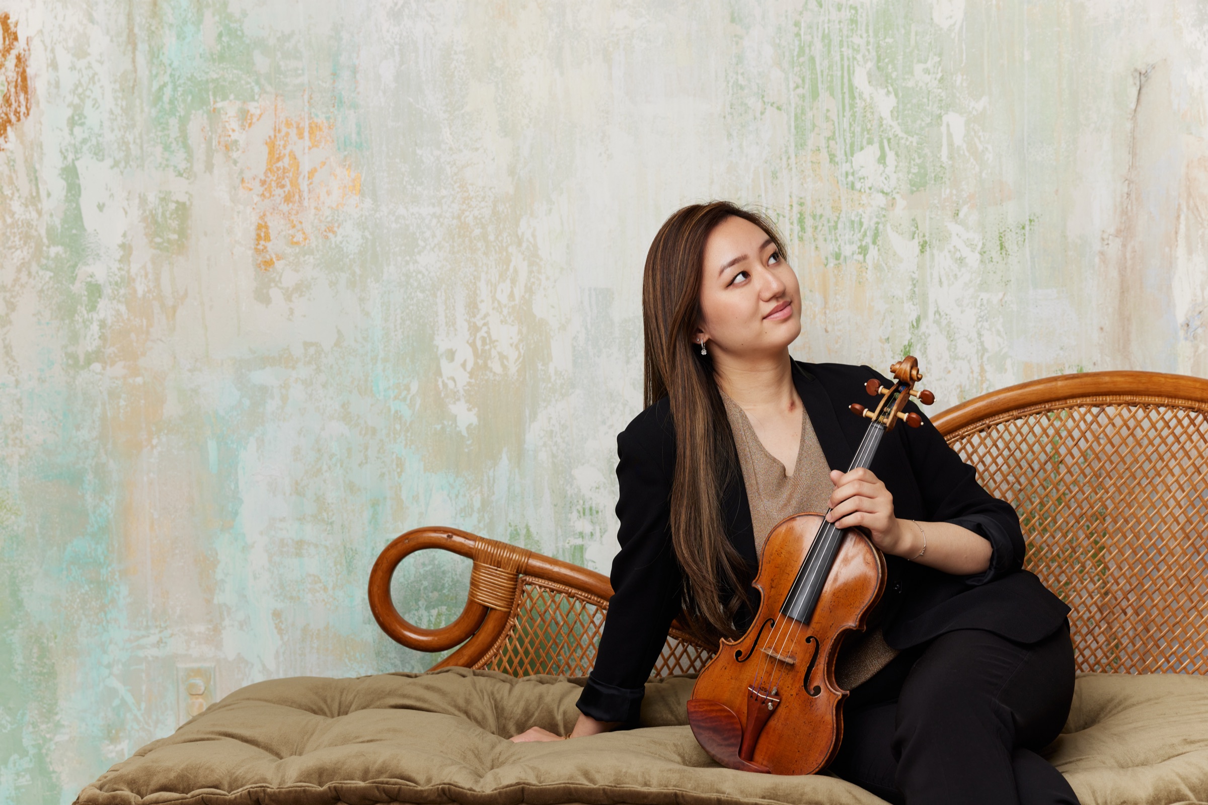 Karen Su seated with her violin against a softly painted wall