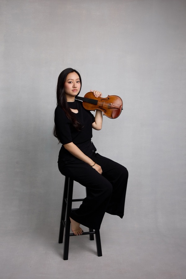 Karen Su seated on a stool, holding her violin at her shoulder